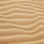 From above of fine wavy yellow sand spreading on smooth surface in hot sunny summer day